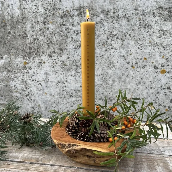 Kalenderlys af bivoks i juledekoration med gran og kogler i tr�fad p� et tr�bord.
